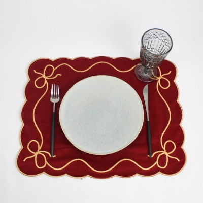Conjunto posto de mesa vermelho com bordados dourados, prato branco, talheres com cabo preto e copo de vidro