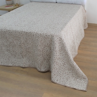 Colcha bege com padrão sobre cama branca num quarto com chão de madeira