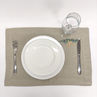 Conjunto de pratos e talheres sobre individual bege com bordado colorido