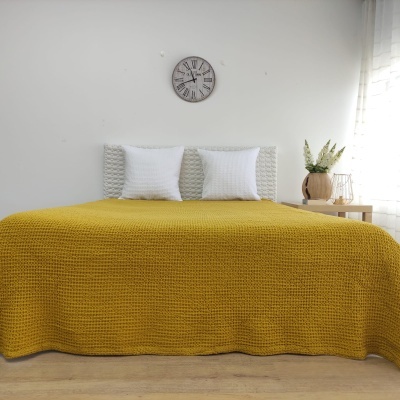 cama com colcha amarela mostarda, almofadas brancas e relógio de parede