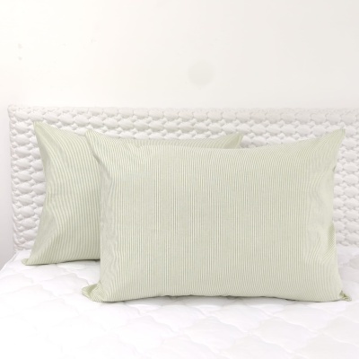 Duas almofadas com fronhas riscas verde-claro e branco sobre colchão branco acolchoado com cabeceira texturizada.