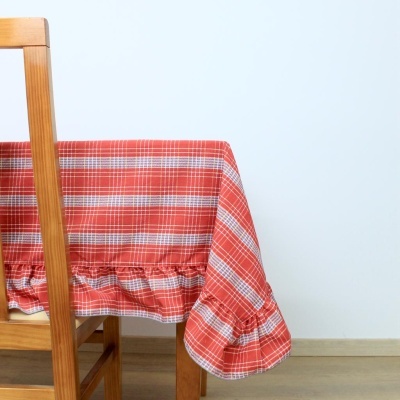 Toalha de mesa vermelha com padrão de quadrados sobre mesa de madeira clara, cadeira e fundo branco