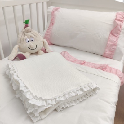 Roupa de cama branca com folhos rosa e peluche de alho num berço