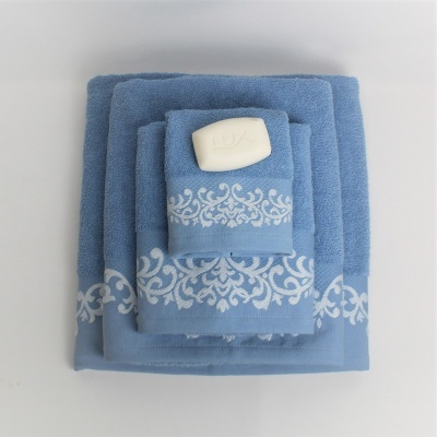 Conjunto de toalhas azuis com padrão branco e sabão Lux em fundo branco