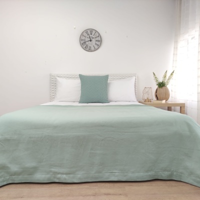 Cama de casal com roupa de cama verde-água e almofadas, relógio na parede e mesa de cabeceira com vaso e flores