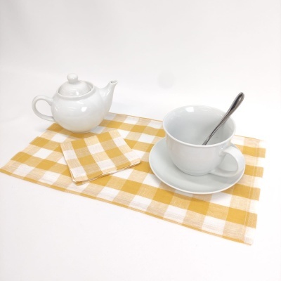 Conjunto de chá com bule e chávena brancos com colher, em cima de toalha xadrez amarela e branca