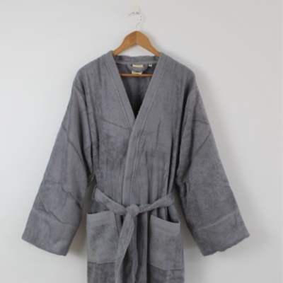 Robe de banho cinzento felpudo com cinto e bolsos, pendurado em cabide de madeira