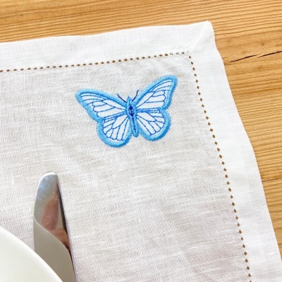 Guardanapo branco com bordado de borboleta azul sobre mesa de madeira