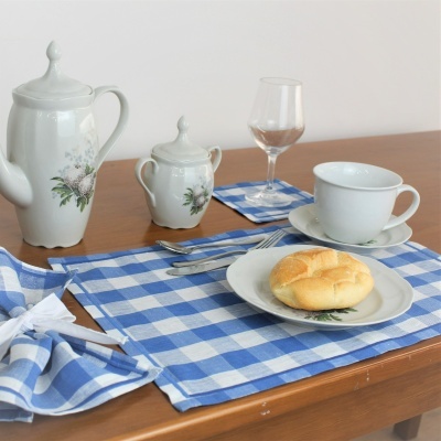 Conjunto de chá em porcelana branca com padrão floral e toalhas xadrez azul e branco sobre mesa de madeira