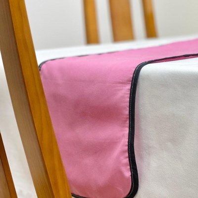Guardanapo cor-de-rosa com borda preta numa mesa branca com cadeiras de madeira