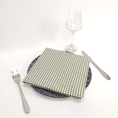 Conjunto de talheres, prato azul com padrão, guardanapo xadrez verde e branco, e taça de vidro