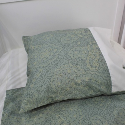 Conjunto de cama para bebé em berço branco com padrão floral verde-azulado e faixa branca