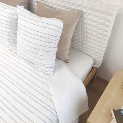 roupa de cama com almofadas riscas e lisa, edredão branco, cabeceira almofadada bege