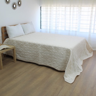 Cama de madeira com colcha branca e almofadas em quarto com cortinas e chão de madeira
