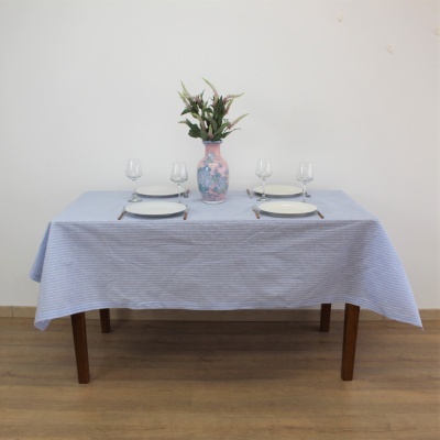 Mesa posta com toalha azul, pratos brancos, copos e vaso com flores