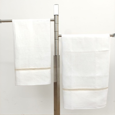 Toalhas de banho brancas com faixa vazada em tons neutros penduradas em suportes metálicos.