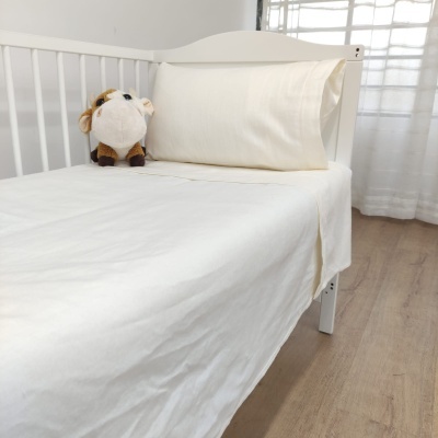 Cama de bebé branca com roupa de cama creme e peluche de vaca