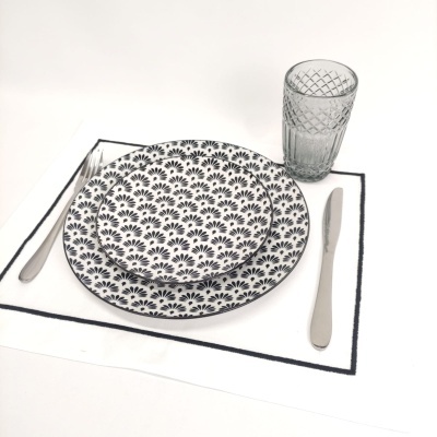 Conjunto de pratos, talheres e copo sobre base branca com borda preta