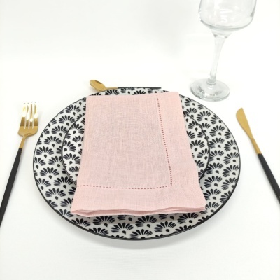 Conjunto de pratos com padrão preto e branco, guardanapo rosa, talheres dourados e copo de vidro