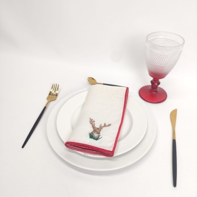 Conjunto de mesa com pratos brancos, guardanapo bordado, talheres pretos e dourados e copo vermelho