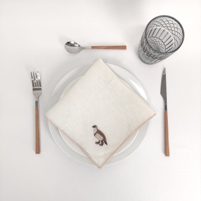 Conjunto de talheres, guardanapo bordado, pratos brancos e copo preto sobre mesa branca