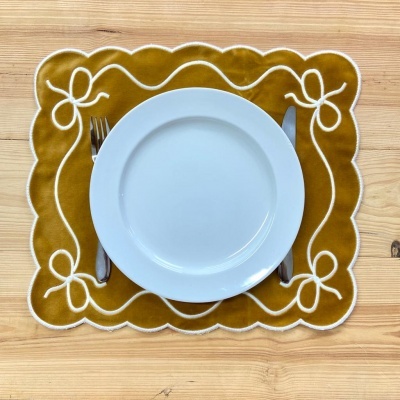 Jogo americano castanho mostarda com prato branco e talheres numa mesa de madeira