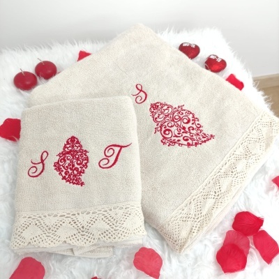 Conjunto de toalhas bege bordadas com detalhes vermelhos e barra de renda em fundo branco com pétalas e velas vermelhas