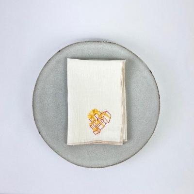 Guardanapo branco com bordado amarelo e rosa sobre prato cinza claro