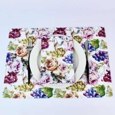 Placemat e guardanapo com padrão floral e cachos de uvas, prato branco, garfo e faca
