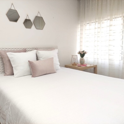 Cama com roupa branca e almofadas rosa e brancas num quarto com decoração clara e minimalista