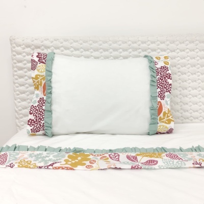 Almofada branca com folhas coloridas e folhos verdes sobre cama branca acolchoada