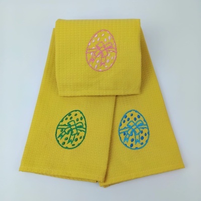 Três toalhas amarelas com bordados de ovos de páscoa em rosa, verde e azul.