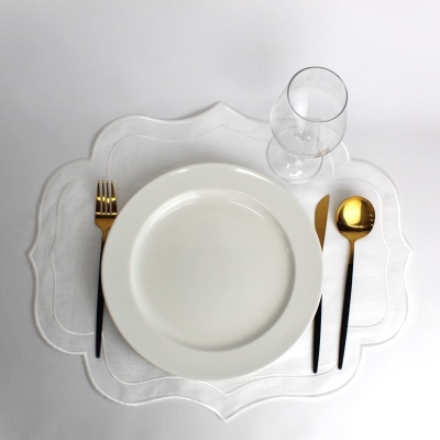 Conjunto de jantar com prato branco, talheres pretos com dourado, copos transparentes e individual branco