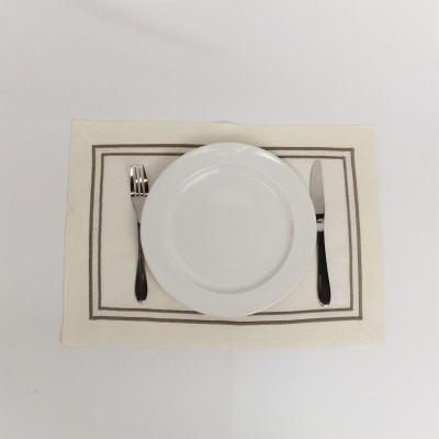 Conjunto de prato branco com garfo e faca sobre individual bege com bordas castanhas.