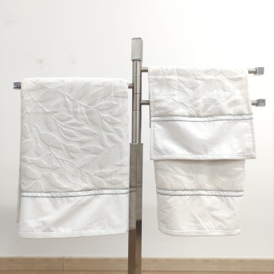 Conjunto de três toalhas de banho brancas com padrão de folhas penduradas em suporte metálico