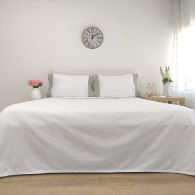 Cama com roupa branca e fronhas verdes em quarto branco com relógio de parede e mesas de cabeceira.