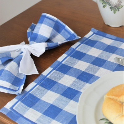 Guardanapo e toalha de mesa azul e branco xadrez sobre mesa de madeira com prato e pão