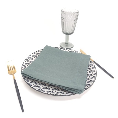 Conjunto de louça com padrão floral preto e branco, guardanapo verde, talheres e copo decorativo