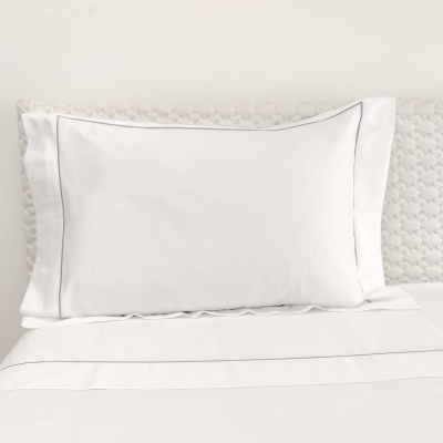 Travesseiro branco com linhas cinzentas sobre cama com lençóis brancos e cabeceira acolchoada