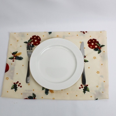 Mesa posta com prato branco, garfo e faca sobre base com padrão natalício