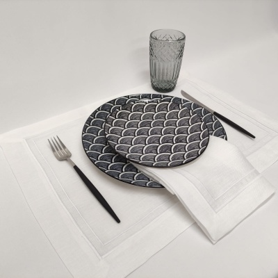 Conjunto de jantar com pratos de cerâmica escamados, faqueiro preto, guardanapo branco e copo de vidro texturizado sobre jogo americano branco