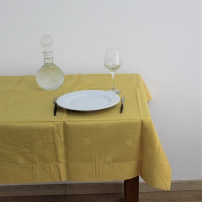 Mesa posta com toalha amarelo mostarda, prato branco, talheres, copo e decantador de vidro.