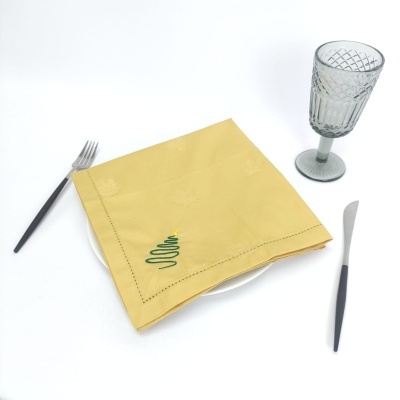 Guardanapo amarelo com bordado de árvore de Natal, prato branco, talheres pretos, taça de vidro cinzenta