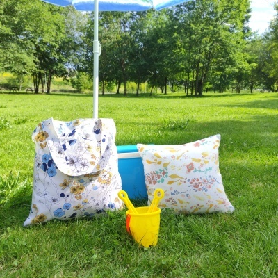 Mochila e almofada florais com balde amarelo e guarda-sol azul na relva de parque