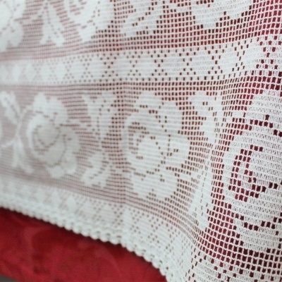 Toalha de mesa branca em renda com padrão de rosas sobre superfície vermelha