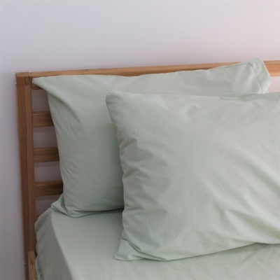 Conjunto de roupa de cama verde claro com fronhas e lençol numa cama de madeira