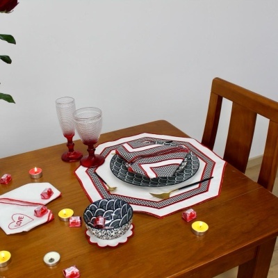 Mesa de madeira decorada com pratos, guardanapos vermelhos e brancos, dois copos altos vermelhos e velas pequenas.