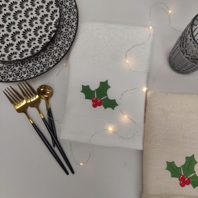 Conjuntos de guardanapos bordados, pratos com padrão preto e branco, talheres dourados e copo transparente num arranjo decorativo