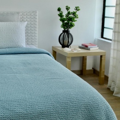 Quarto com cama e mesa de cabeceira, cobertor azul claro e almofada branca