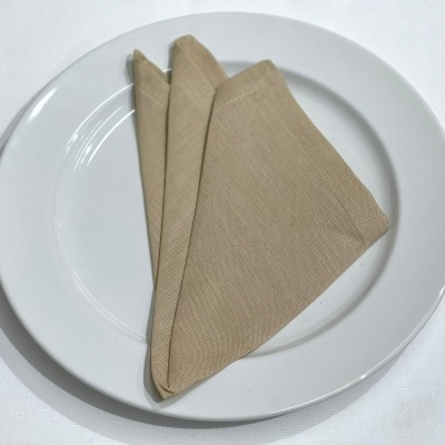 Guardanapo bege dobrado sobre prato branco em mesa com toalha branca
